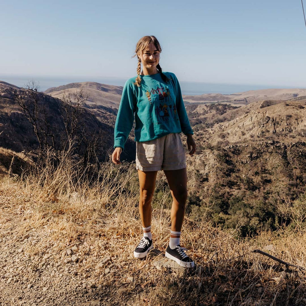 Women's Monterey Sneaker in Black canvas, worn with shorts by a person standing on a hillside trail