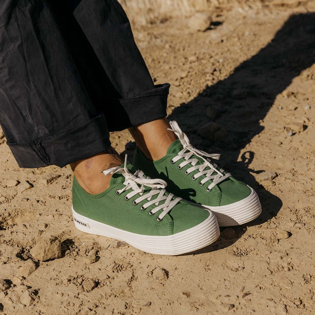 Women's Monterey Sneaker in Cactus canvas, close-up worn with black pants on sandy ground