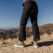 Women's Monterey Sneaker in Cactus canvas, worn with dark cuffed pants on a hillside