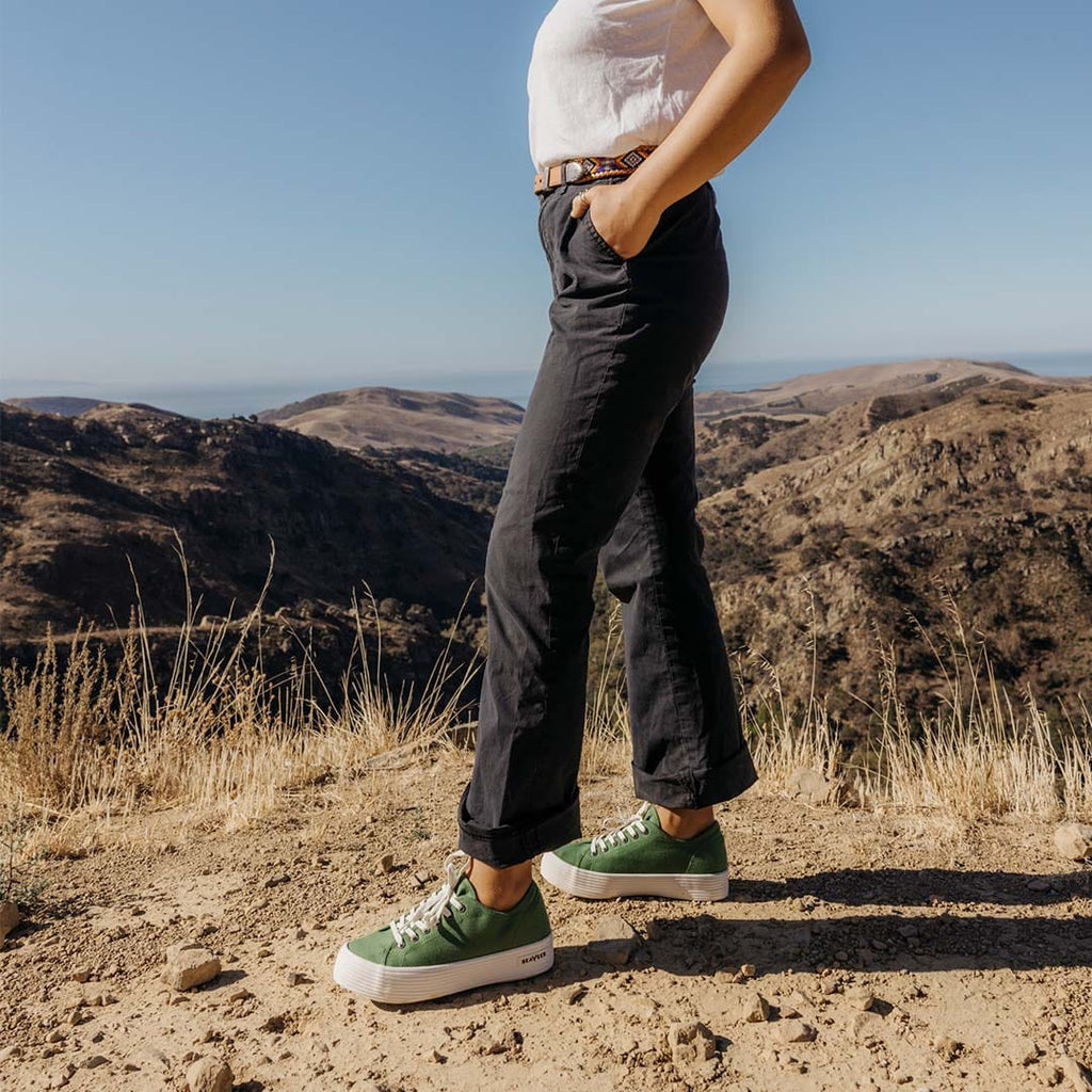 Women's Monterey Sneaker in Cactus canvas, worn with black pants on a hilltop trail