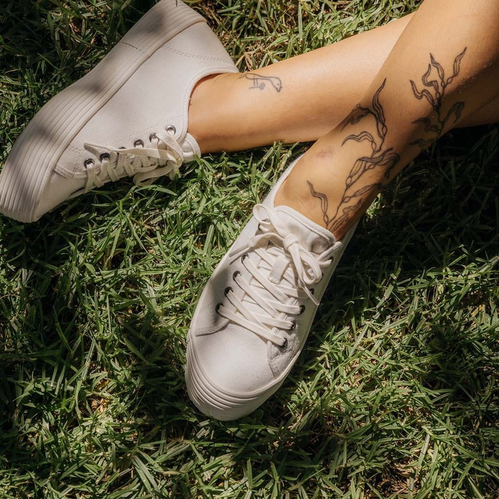 Women's Monterey Sneaker in Bleach canvas, viewed from above, worn with bare ankles on grass