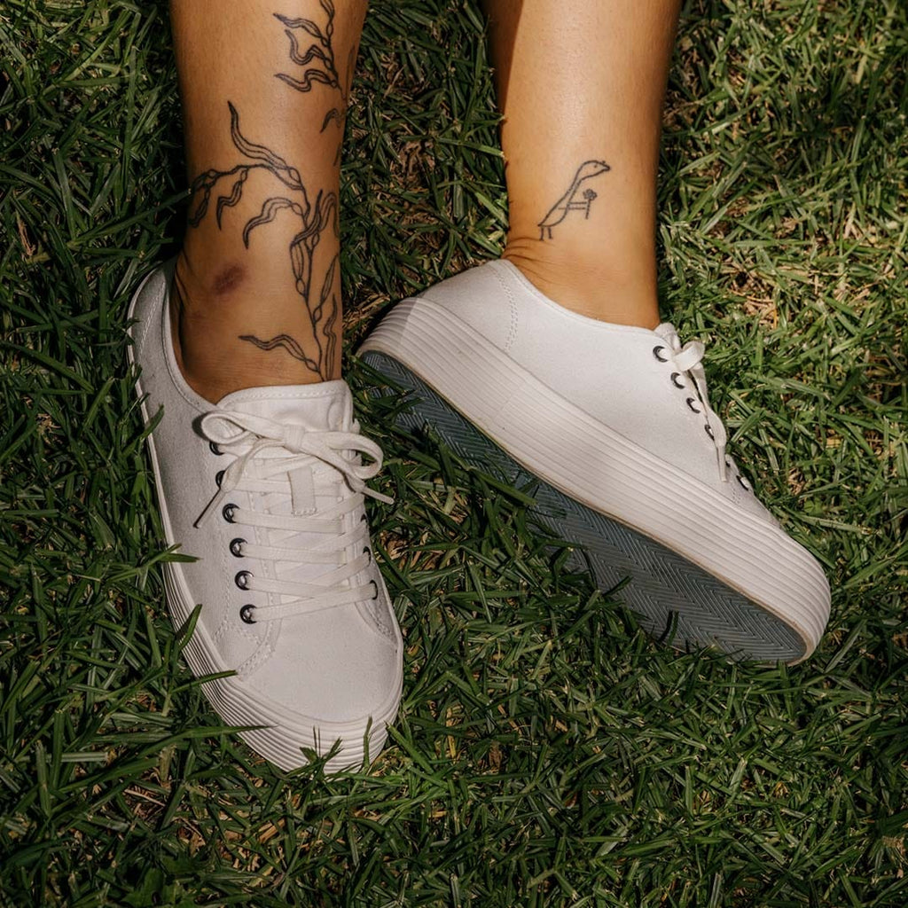 Women's Monterey Sneaker in Bleach canvas, close-up of both shoes, worn with bare ankles on grass