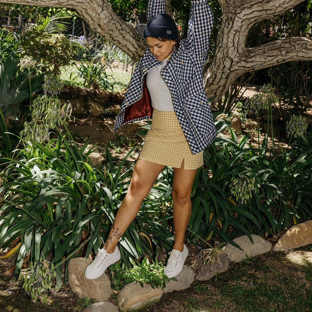 Women's Monterey Sneaker in Bleach canvas, worn with a khaki skirt by a person standing among bushes