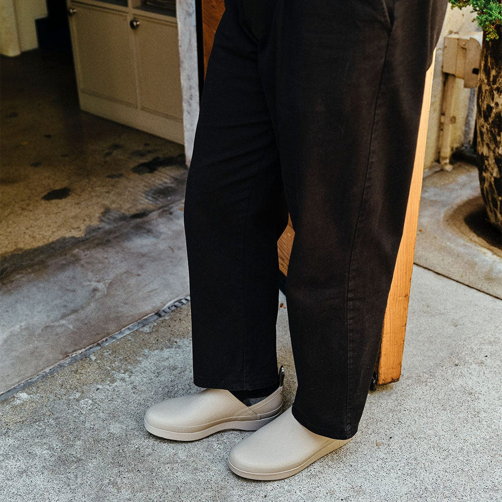 Men's Calistoga Clog in Concrete rubber, worn with black pants on a concrete step