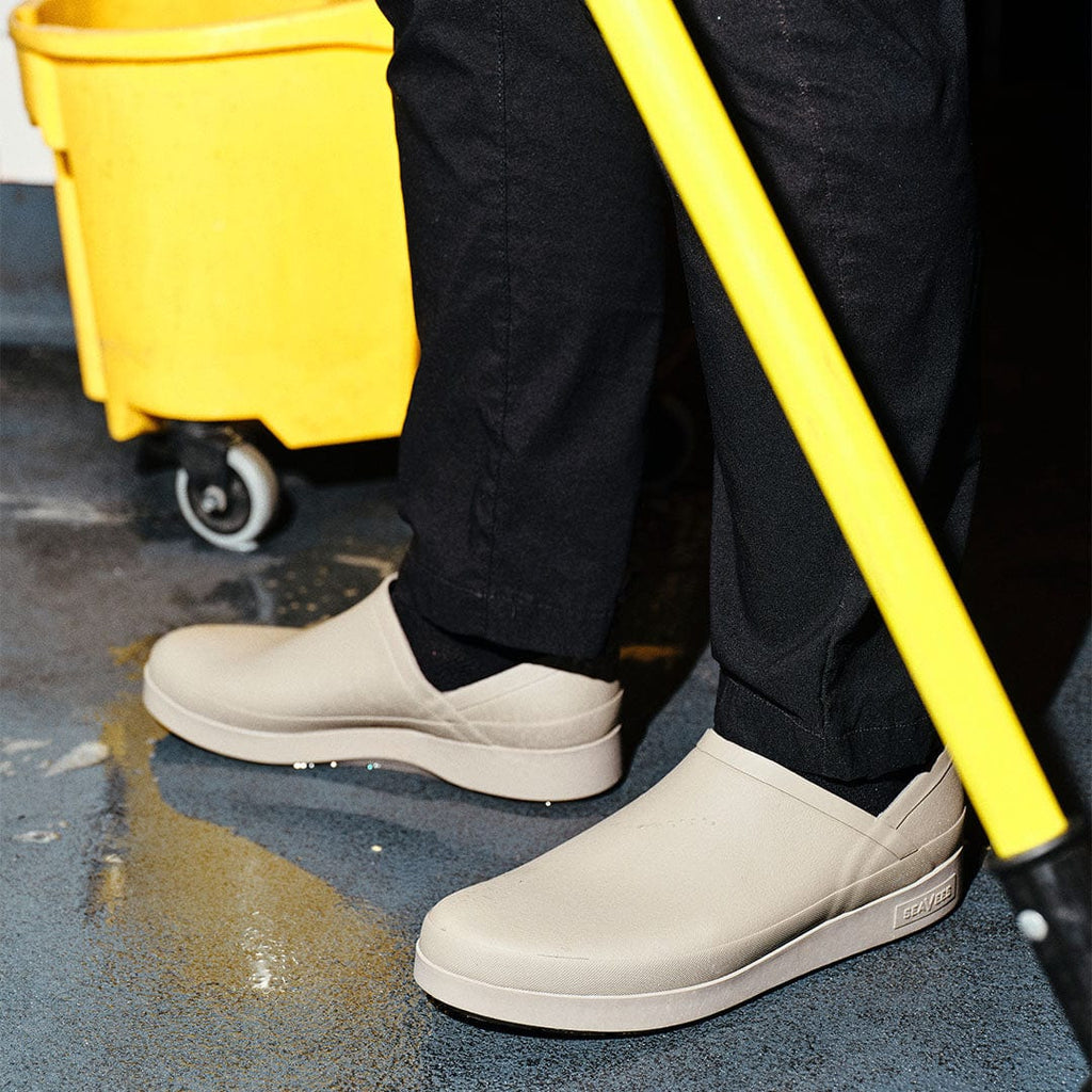 Women's Calistoga Clog in Concrete rubber, worn with black pants in a kitchen beside a mop bucket