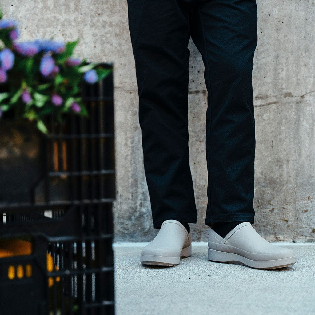Women's Calistoga Clog in Concrete rubber, worn with black pants on a sidewalk beside a crate