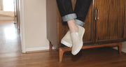 Men's Baja Slip On in Natural canvas, worn with cuffed jeans, standing in a wood-floored hallway