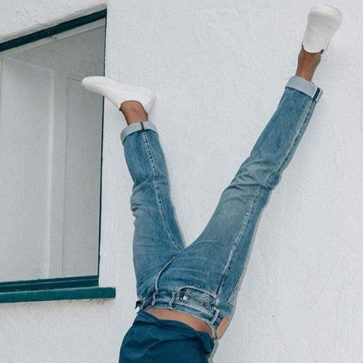 Men's Hawthorne Slip On in Bleach fabric, worn with cuffed jeans, feet raised against a white wall