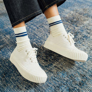 Women's Sato Oxford in Parchment canvas, worn with striped socks on a blue rug, front view