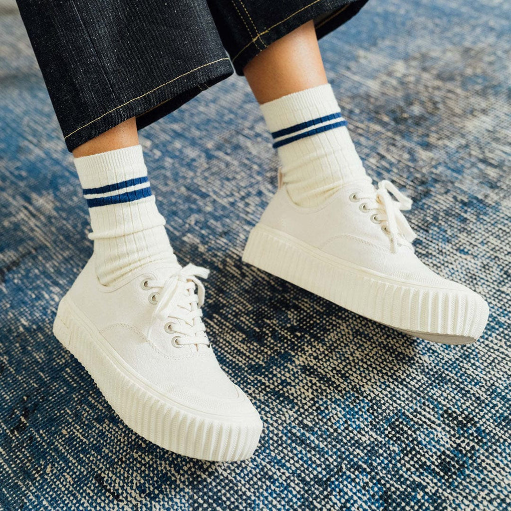 Women's Sato Oxford in Parchment canvas, worn with striped socks on a blue rug, front view