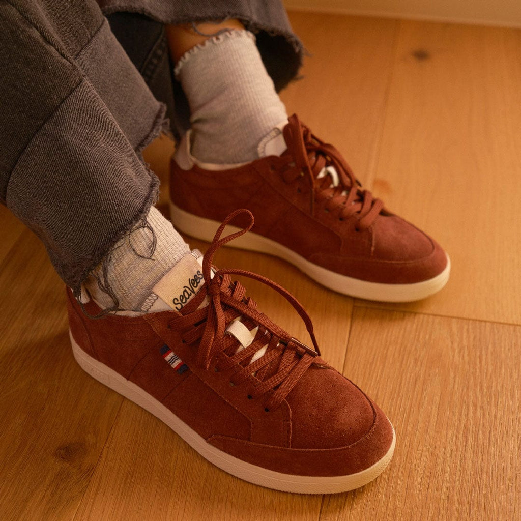 Women's Clipper Sneaker in Plum suede, worn with socks on a wood floor, pair from above