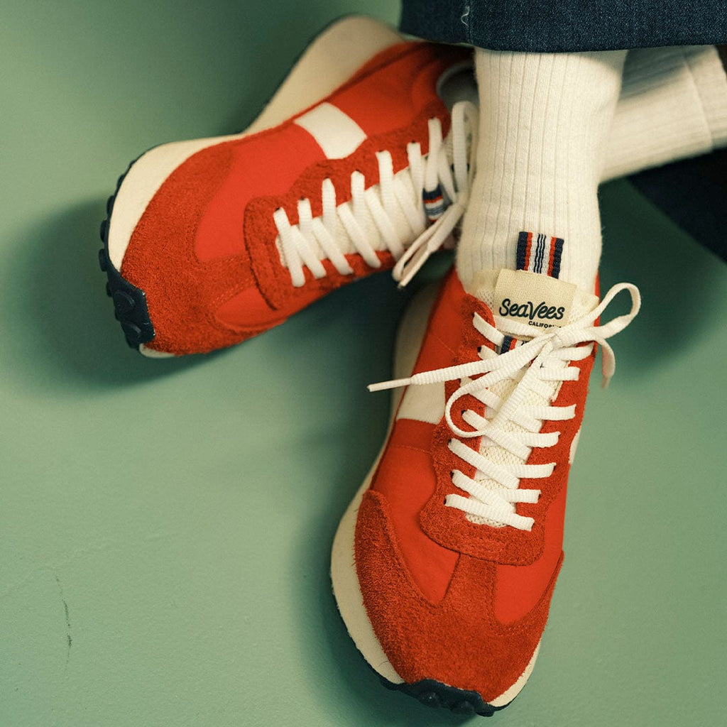 Women's Acorn Trainer sneaker in Candy Apple Red nylon and suede, worn with white socks on a teal floor, pair from above