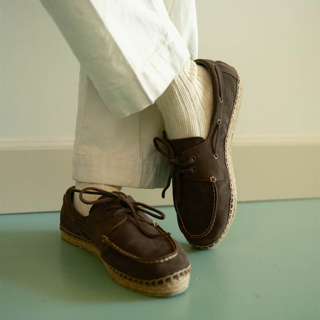 Men's Carmel Loafer in Dark Chocolate suede, worn with white pants and socks on a pale green floor