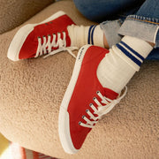Women's Monterey Sneaker in Forever Red canvas, worn with cream socks on a shearling seat, side view