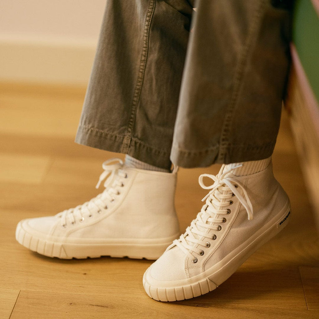 Men's La Brea Lug in White canvas, worn with olive pants on a wood floor