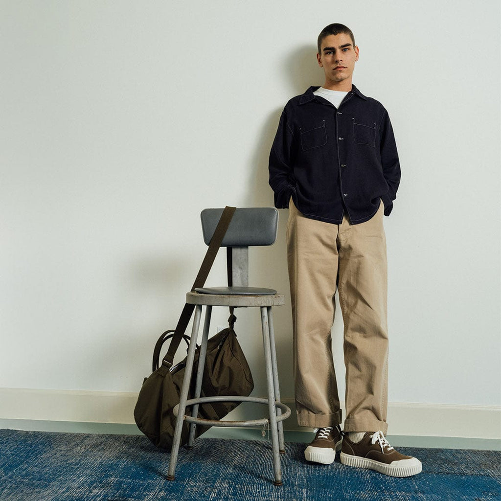 Men's Sato Oxford in Brownstone canvas, worn by a man standing beside a stool