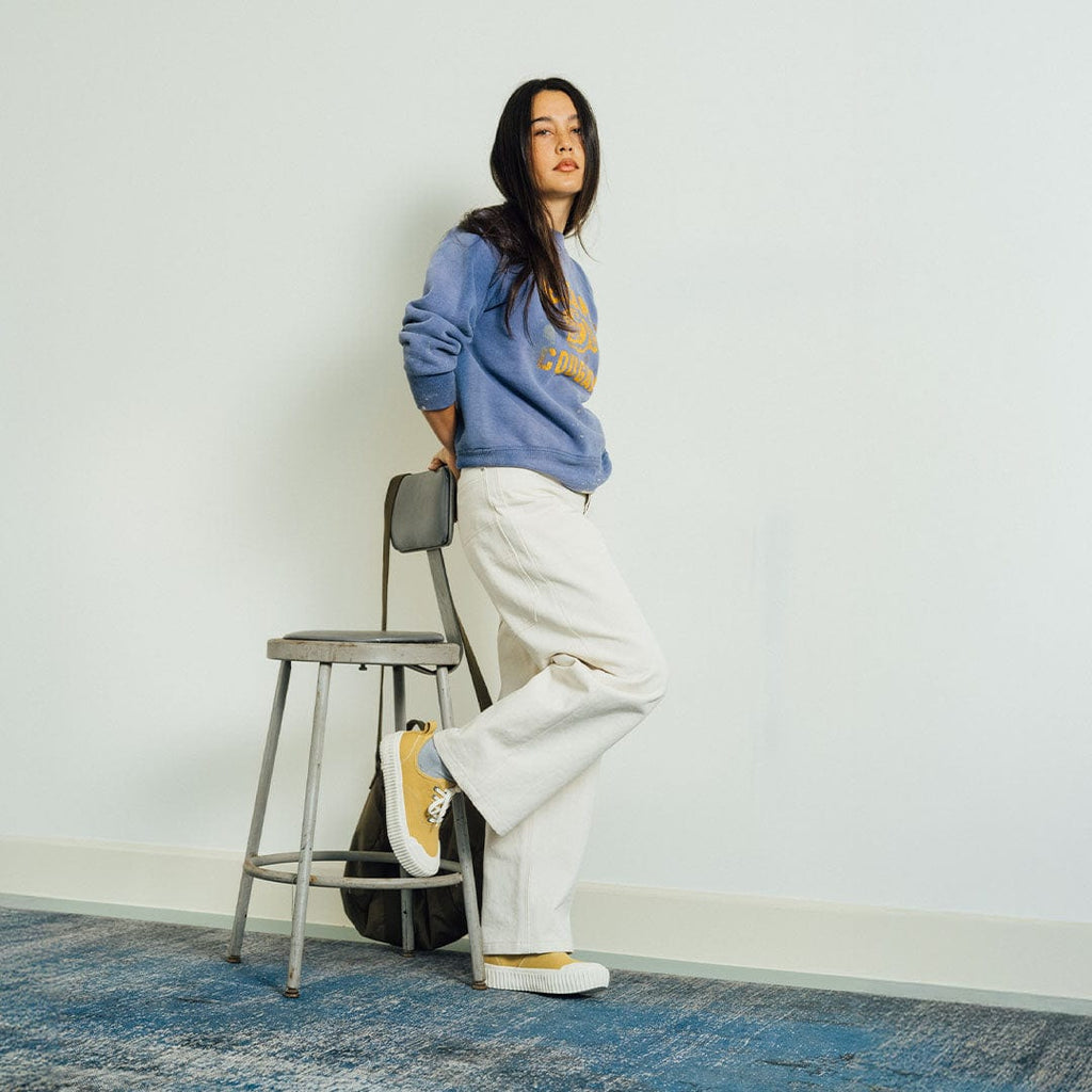 Women's Sato Oxford in Dijon canvas, worn by a woman standing beside a metal stool