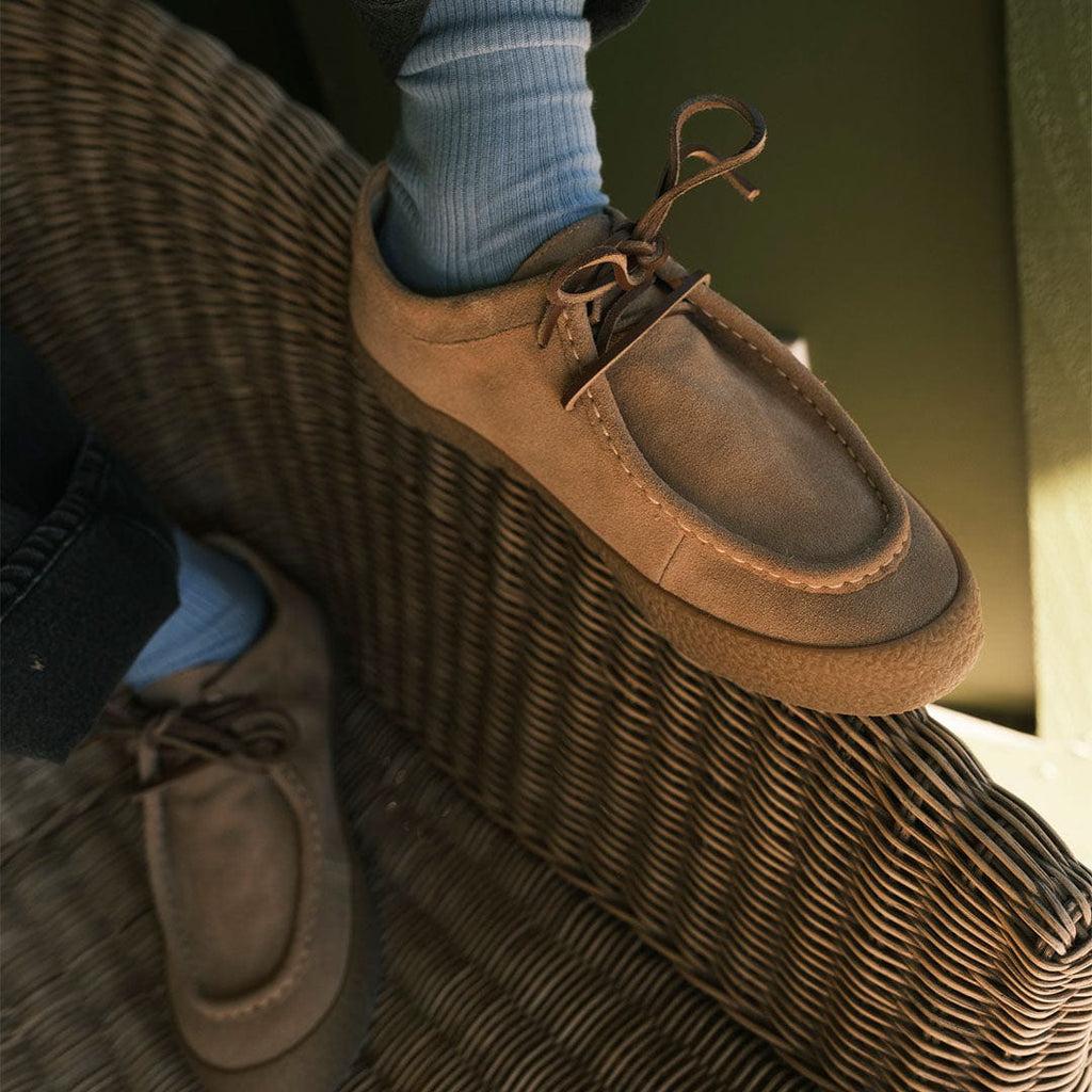 Men's Hayward Loafer in Tan suede, worn with blue socks, one foot raised on a wicker chair, close up
