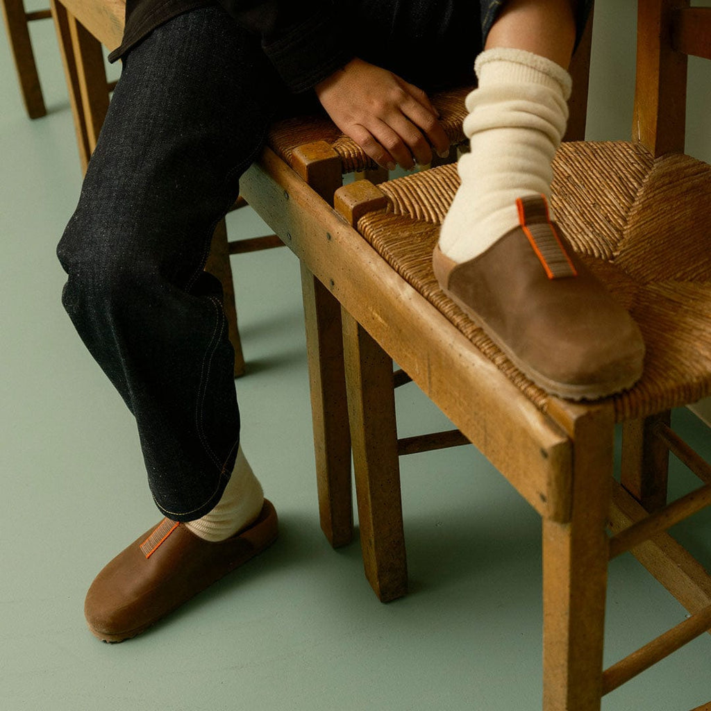 Women's Tiburon Trekker sandal in Elmwood leather, worn with cream socks on a wooden chair, side view