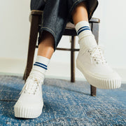 Women's Sato Oxford in Parchment canvas, worn with striped socks on a wooden chair, side view