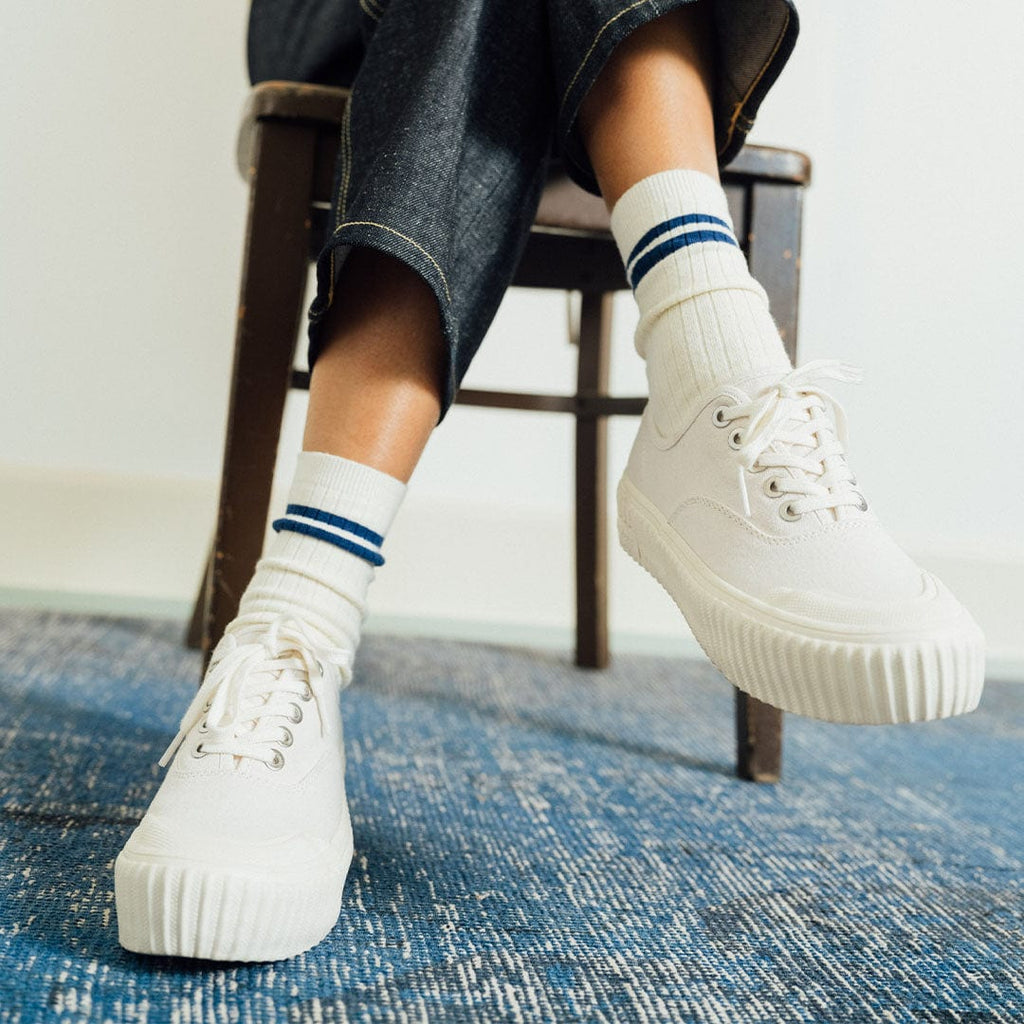 Women's Sato Oxford in Parchment canvas, worn with striped socks on a wooden chair, side view