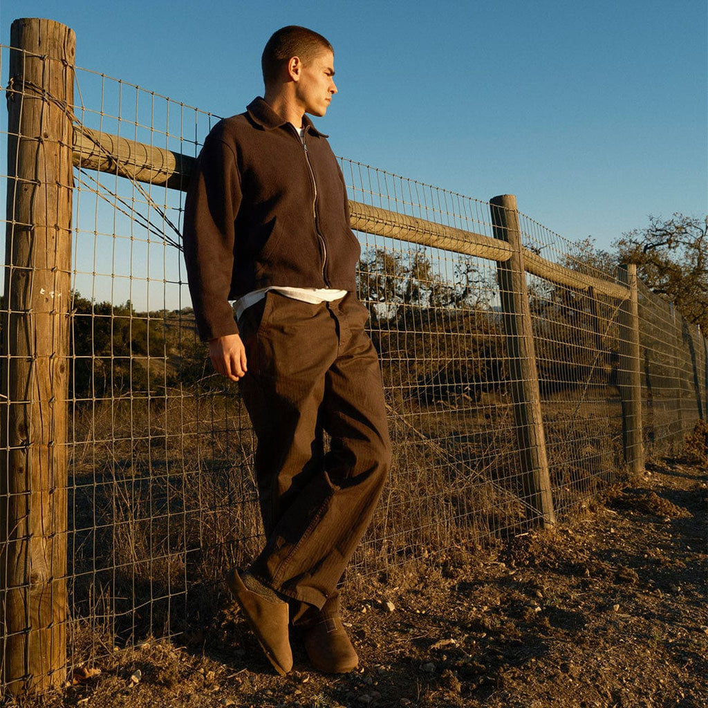 Men's Tiburon Trekker sandal in Fossil leather, worn by a man standing at a wooden fence