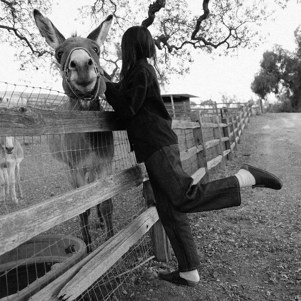 Women's Tiburon Trekker sandal in Elmwood leather, black and white shot of a woman leaning on a fence beside a donkey