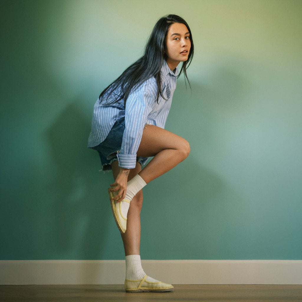 Women's Miramar Espadrille in Butter mesh, worn by a woman standing on one leg against a teal wall