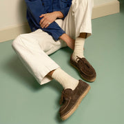 Men's Carmel Loafer in Dark Chocolate suede, worn by a person reclining on a pale green floor in cream pants