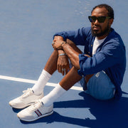 Men's Royal Runner sneaker in White nylon and suede, worn with white socks by a person seated on a tennis court