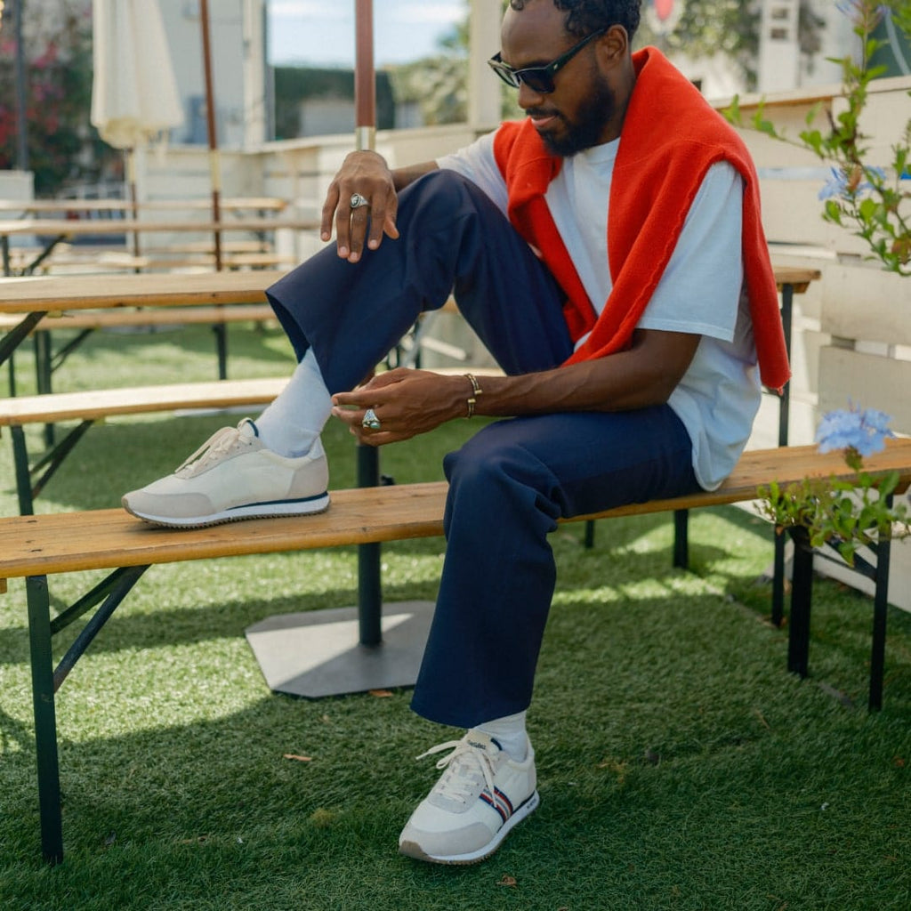 Men's Royal Runner sneaker in White nylon and suede, worn with navy pants by a person seated at a picnic table