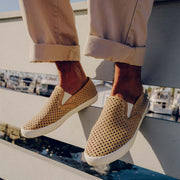 Men's Baja Slip On in Cloud vegan nubuck, worn with cuffed khaki pants, feet raised over a marina