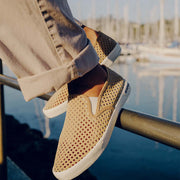 Men's Baja Slip On in Cloud vegan nubuck, worn with cuffed khaki pants by a marina railing, close up