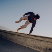 Men's Baja Slip On in Cloud vegan nubuck, worn by a person mid-jump over a concrete wall