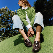Women's Rickie Tassel Loafer in Dark Chocolate leather, worn by a person seated on grass in a green cardigan