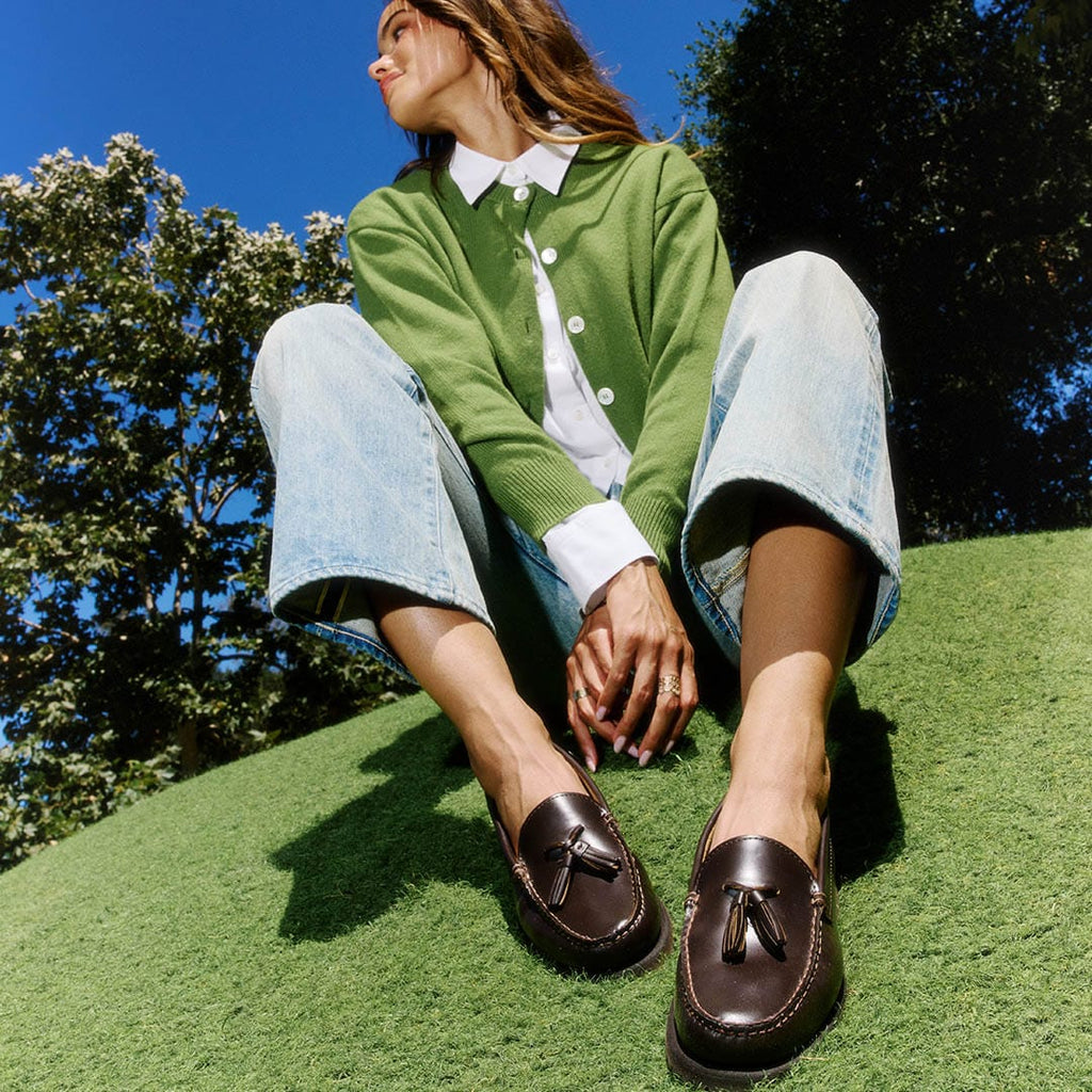 Women's Rickie Tassel Loafer in Dark Chocolate leather, worn by a person seated on grass in a green cardigan