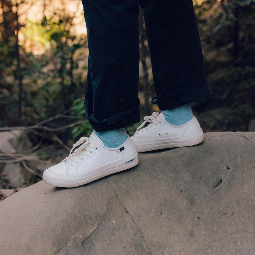 Women's SeaChange LTT sneaker in White Corn Leather, worn with cuffed navy pants and teal socks on a rock ledge