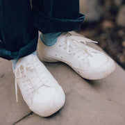 Women's SeaChange LTT sneaker in White Corn Leather, close-up worn with teal socks on a rock ledge