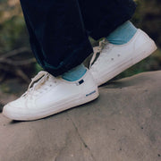 Women's SeaChange LTT sneaker in White Corn Leather, side close-up worn with teal socks on a rock ledge