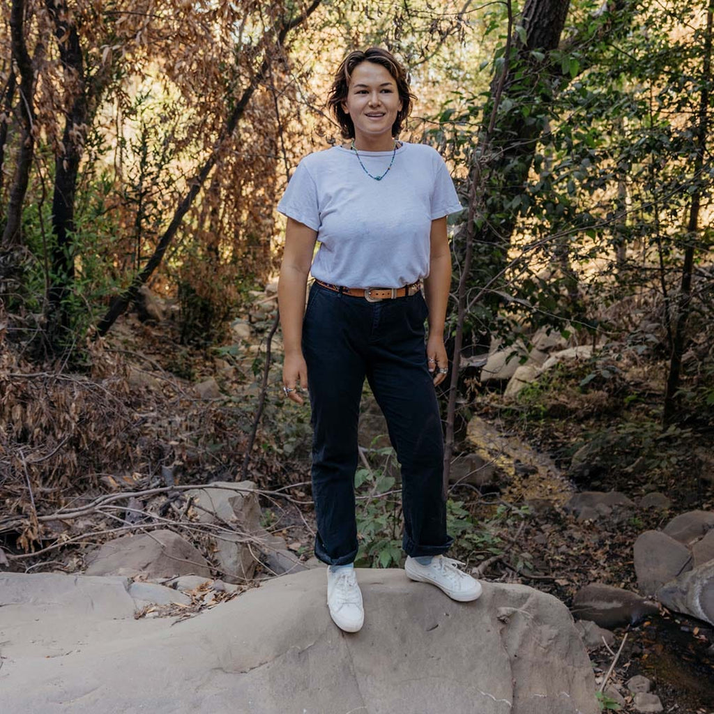 Women's SeaChange LTT sneaker in White Corn Leather, worn with dark pants, full-length view on a rock in the woods