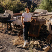 Women's SeaChange LTT sneaker in White Corn Leather, worn with dark pants by a person standing among rusted vintage cars