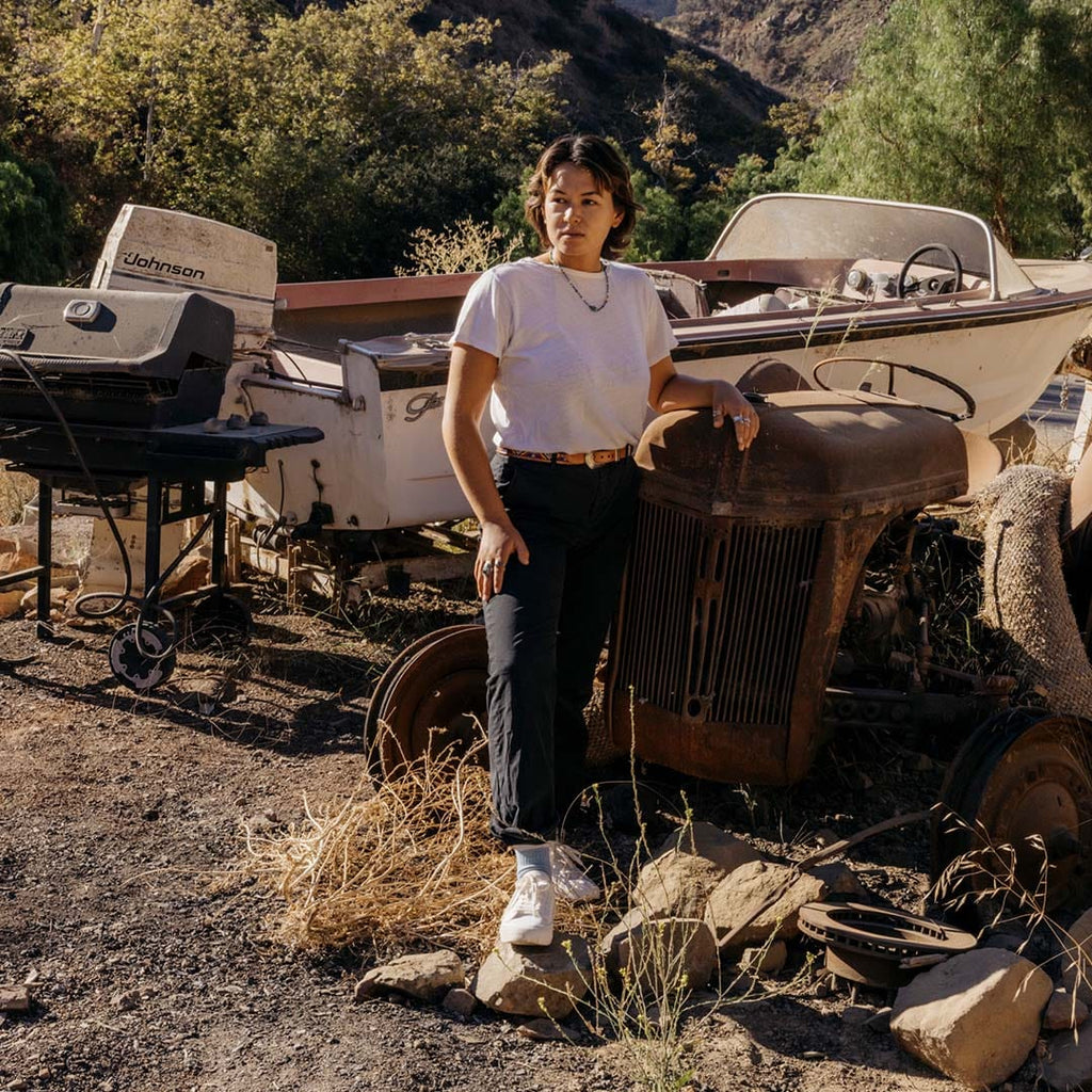 Women's SeaChange LTT sneaker in White Corn Leather, worn with dark pants by a person standing among rusted vintage cars