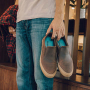 Men's Hawthorne Slip On in Kona leather, pair held in hand by a person standing at a staircase