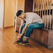 Men's Hawthorne Slip On in Kona leather, worn with jeans by a person seated on a staircase tying a shoe
