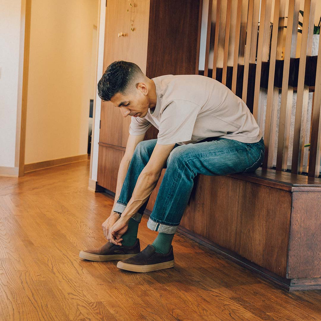 Men's Hawthorne Slip On in Kona leather, worn with jeans by a person seated on a staircase tying a shoe