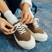 Women's Sato Oxford in Brownstone canvas, close-up of hands tying the white laces on a blue rug