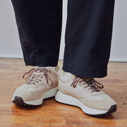 Women's Acorn Trainer sneaker in Cream Cafe nylon and suede, worn with dark pants on a wood floor
