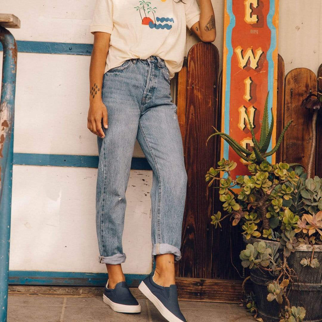 Women's Hawthorne Slip On in True Navy fabric, worn with cuffed jeans, full-length view in front of a mural