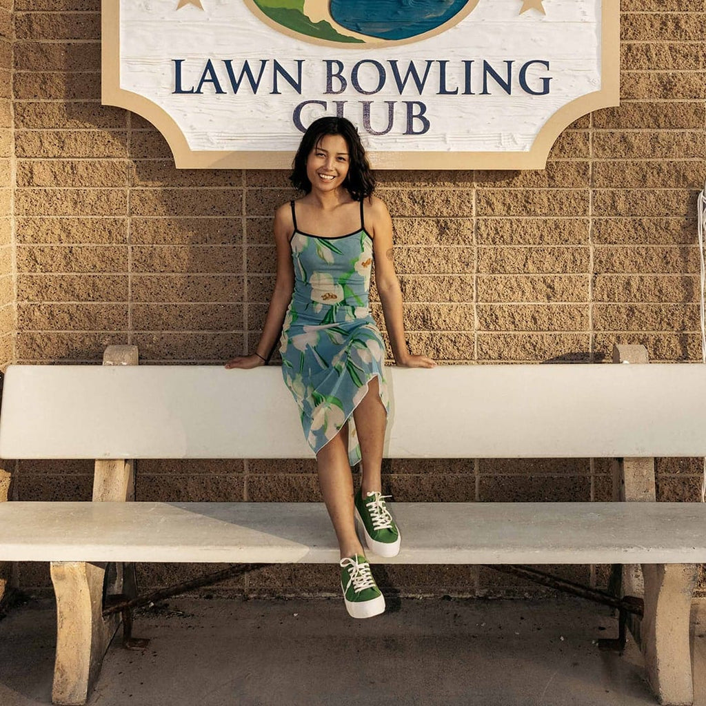 Women's Monterey Sneaker in Cactus canvas, worn with a printed dress by a person seated on a bench