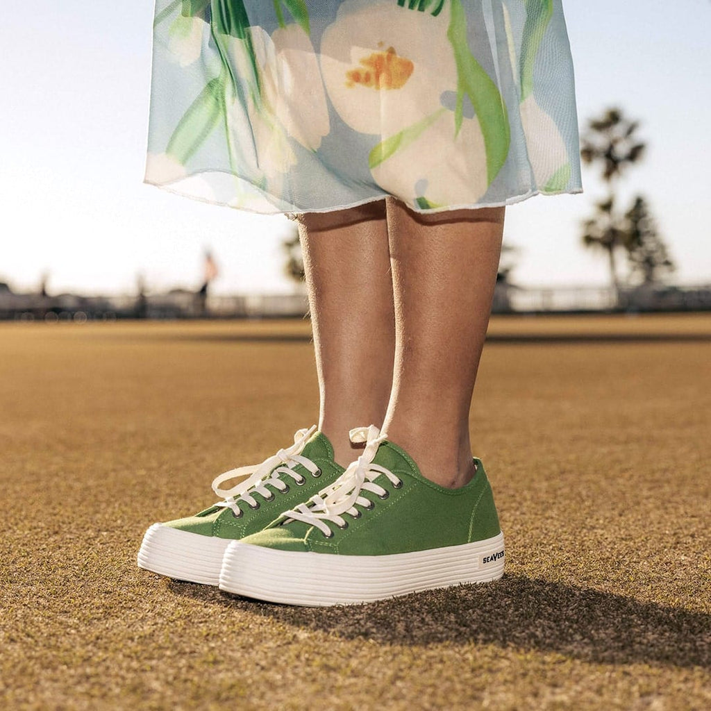 Women's Monterey Sneaker in Cactus canvas, close-up worn with a floral skirt on a dirt field